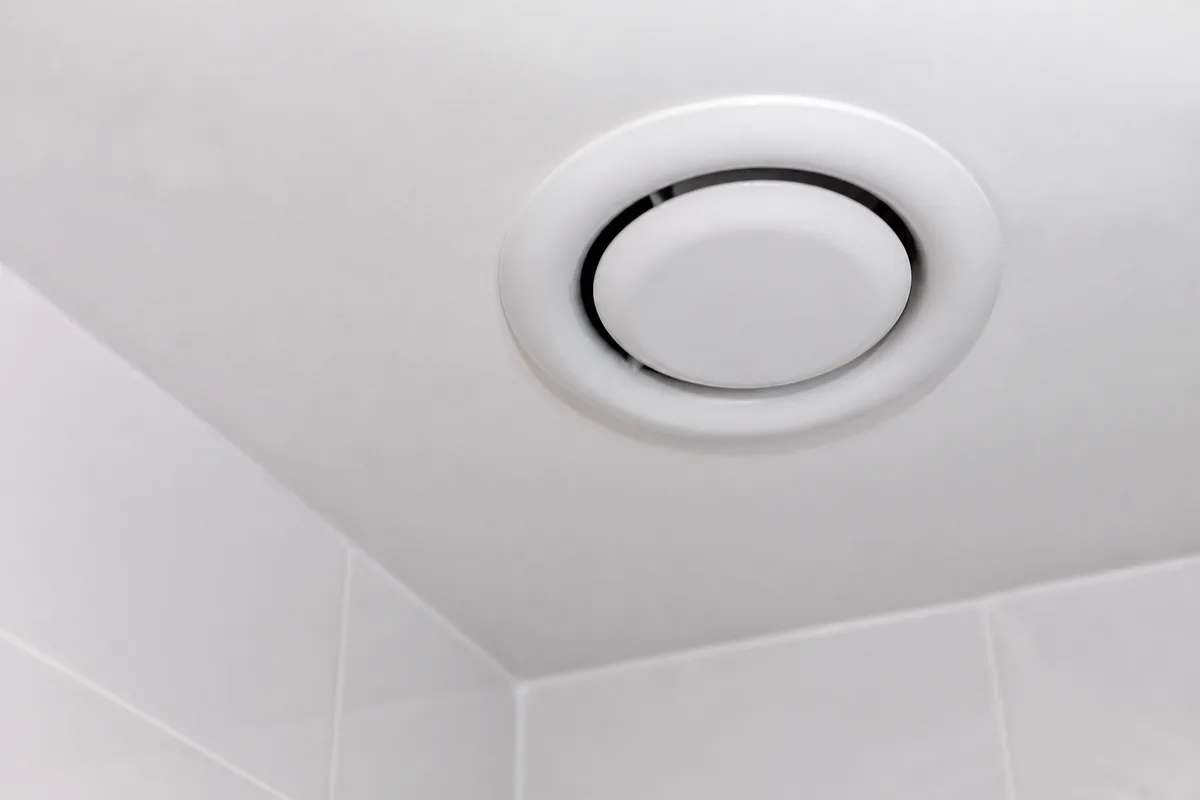 Bouche d&rsquo;extraction ronde encastrée dans un plafond de salle d&rsquo;eau carrelée