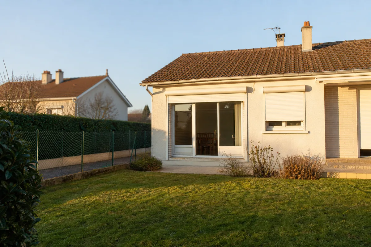 Pavillon de plain-pied des années 1970 vu depuis son jardin étroit bordé d’une clôture mitoyenne