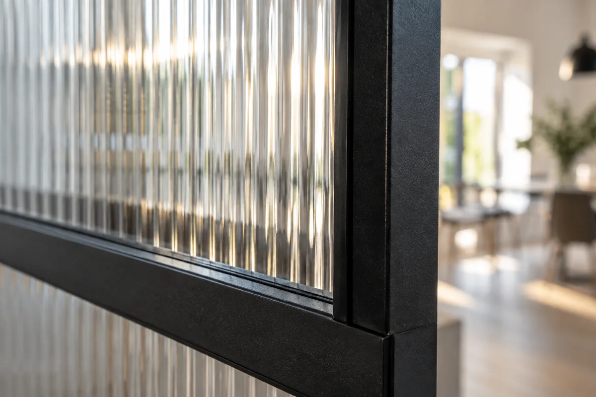 Détail d&rsquo;un profilé en acier noir encadrant un verre cannelé